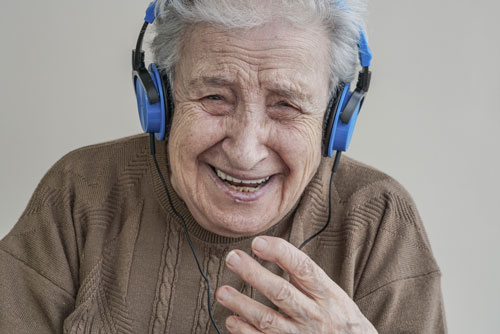 Seniorin hat Kopfhörer auf und lacht herzhaft