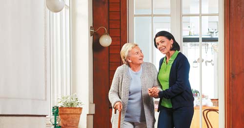 Pflegekraft stützt und begleitet Seniorin
