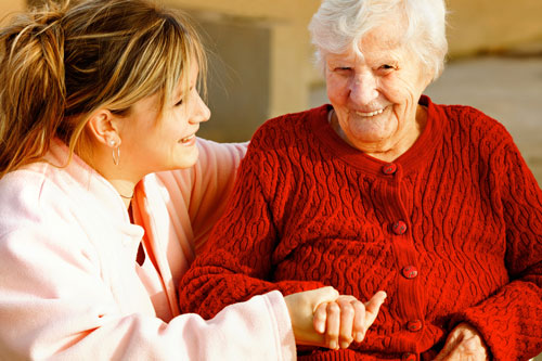 Betreuungskraft hält die Hand einer Seniorin und lächelt