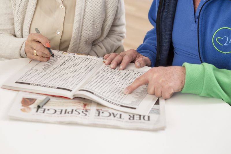 Betreuungskraft und Seniorin lösen zusammen Kreuzworträtsel.