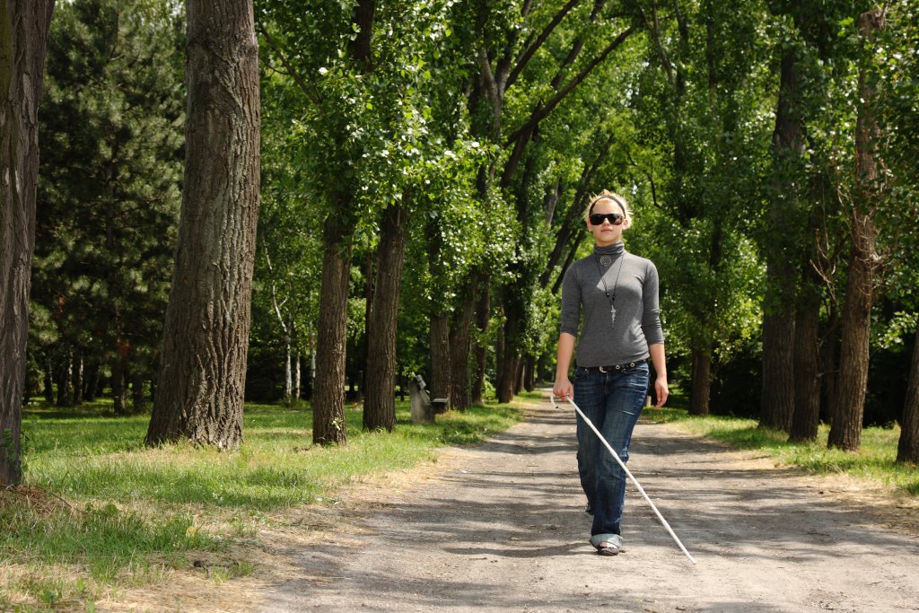 Blinde Frau mit Blindenstock beim Spazieren durch den Wald