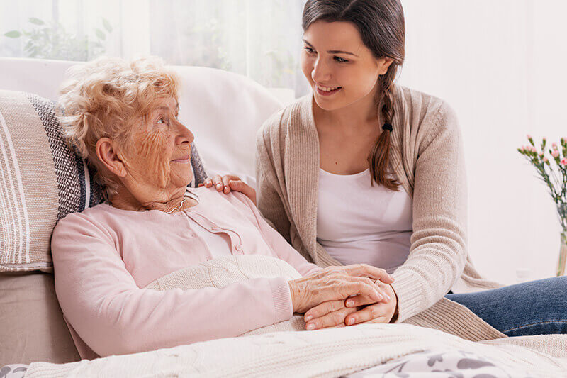 Betreuungskraft hält einer bettlägerigen Seniorin die Hand