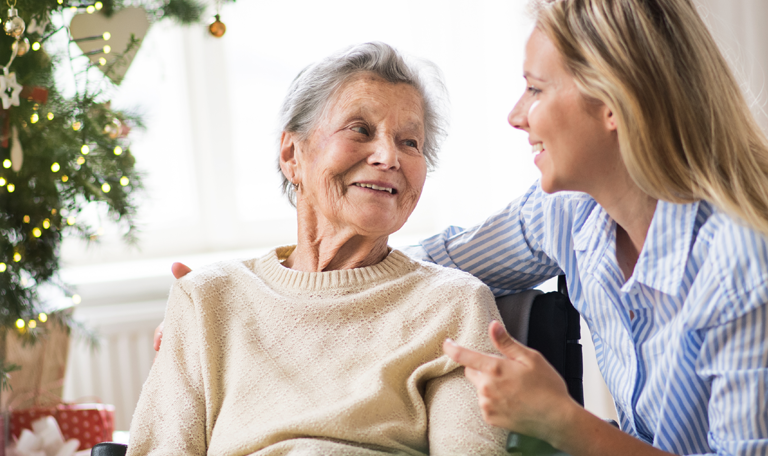 Seniorin und Betreuungskraft vor dem Weihnachtsbaum