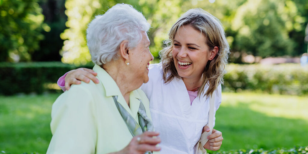 Oma lacht mit Pflegerin im Arm