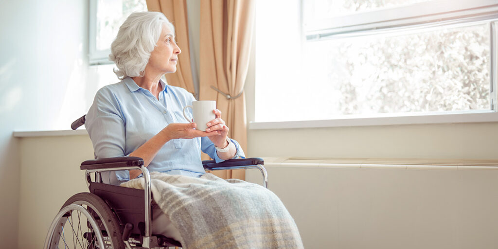Ältere Frau im Rollstuhl schaut aus einem Fenster.