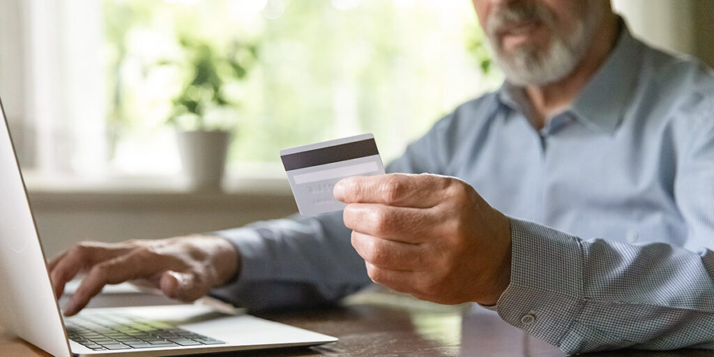 Alter Mann sitzt an Arbeitstisch und schaut auf Kreditkarte